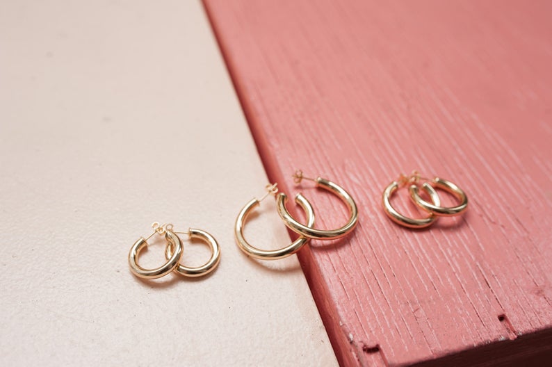 Three pairs of varying-sized gold hoop earrings rest neatly on a dual-toned pink and cream surface.