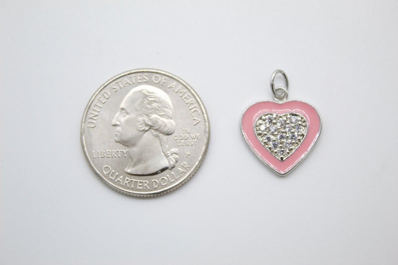 A small pink enamel heart pendant with pavé crystal details rests beside a US quarter for scale.