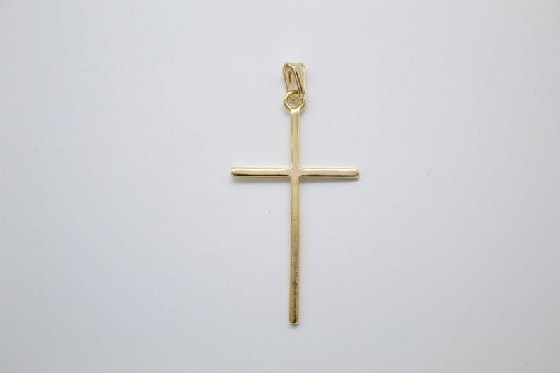 A polished gold cross pendant hangs against a plain white background.