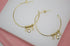 A pair of gold hoop earrings features dangling cubic zirconia charms on a white display surface.
