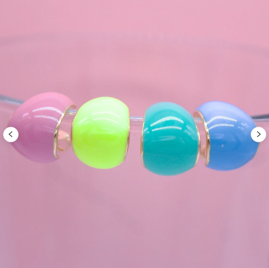 Four colorful enamel dome hoop earrings in pink, lime green, turquoise, and blue line up horizontally against a pastel pink background.