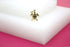 A gold turtle pendant rests on a white display block against a pink background.