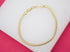 A delicate gold snake chain bracelet rests in a circle on a white display surface against a bright pink background.