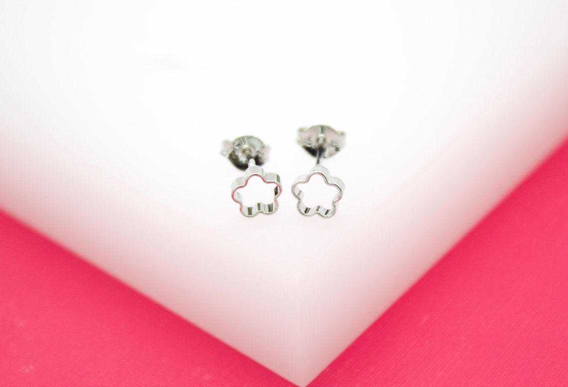 A pair of silver flower stud earrings rests on a white display block.