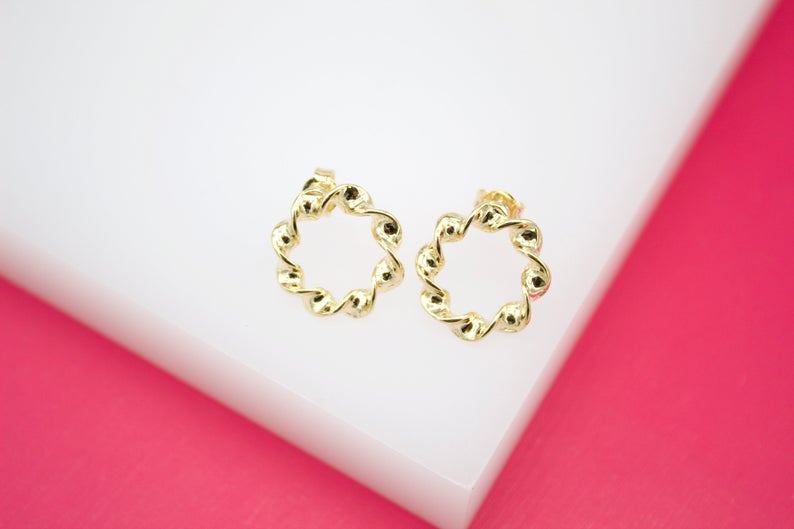 A pair of twisted gold hoop earrings rests against a white and pink background.