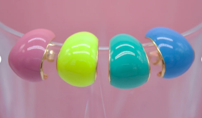 Four vibrant, glossy enamel hoop earrings in pink, lime green, teal, and blue line up against a soft pink background.