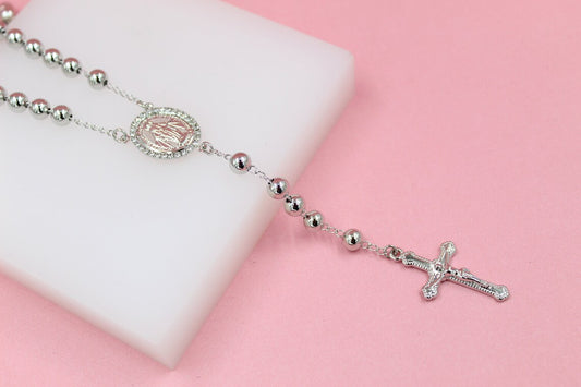 A sparkling silver rosary necklace with a pink centerpiece and crucifix rests on a white display block against a soft pink background.