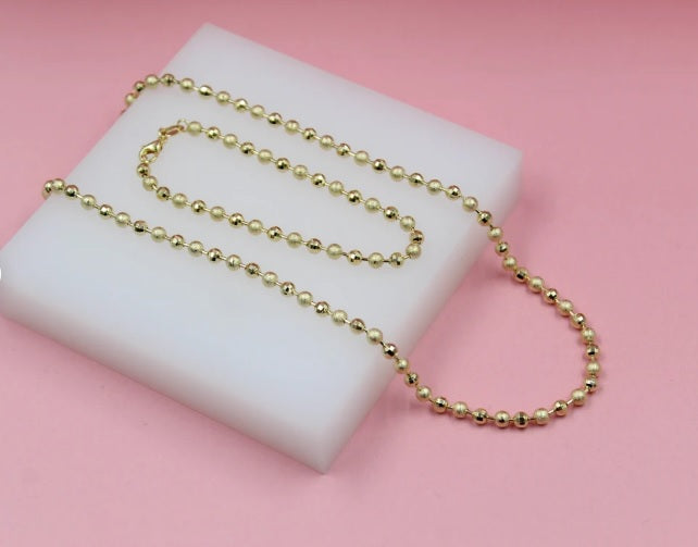 A shiny gold ball chain rests on a white display pad against a pink background.