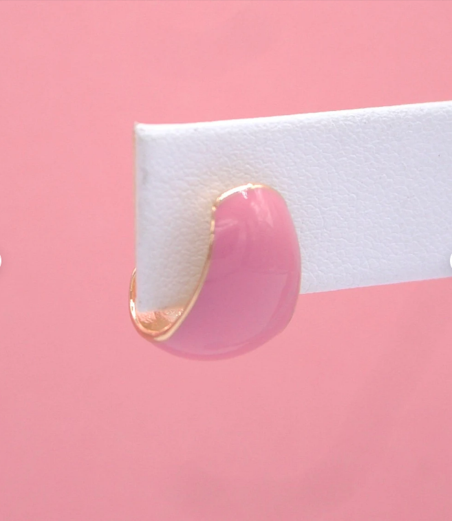 A glossy pink enamel hoop earring with gold trim rests on a white display card against a soft pink background.