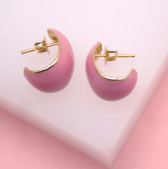 A pair of pink enamel dome hoop earrings resting on a white display stand against a soft pink background.