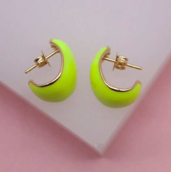 A pair of neon green enamel hoop earrings with gold backing rests on a pink and white display surface.