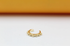 A shiny gold-plated ear cuff rests on a white surface, showcasing a beaded texture along its curved edge.
