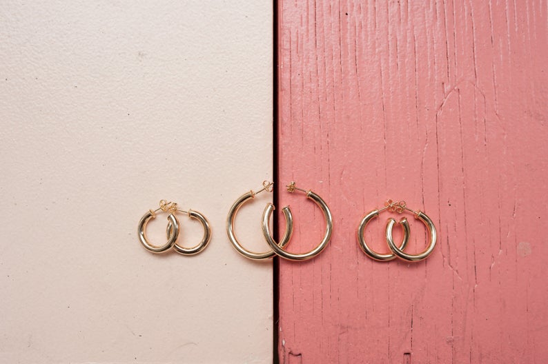 Three pairs of gold hoop earrings in varying sizes rest on a split cream and pink wooden surface.