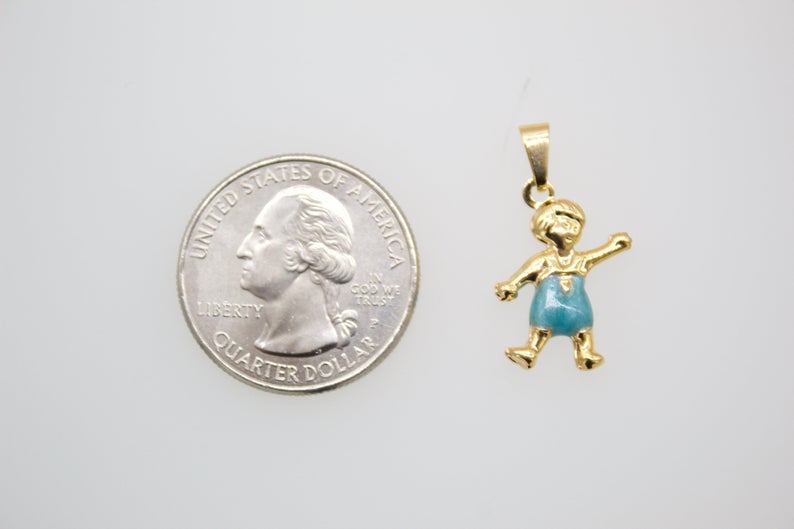 A gold boy charm pendant with blue enamel shorts rests next to a US quarter for size comparison.