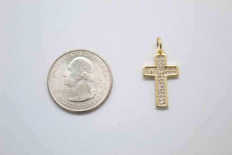 A gold pave rhinestone cross charm rests next to a US quarter coin for size comparison.
