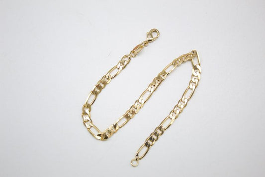 A gold Figaro chain lies in a curved shape against a plain white background.