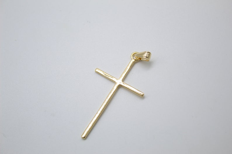 A polished gold cross pendant rests on a neutral light gray background.