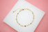 A delicate gold chain bracelet features alternating heart charms and sparkling zirconia stones on a white and pink display surface.
