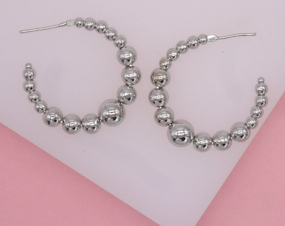 A pair of shiny silver beaded hoop earrings rests against a light background.