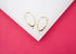 Two gold leverback earring findings with open loops rest on a white surface against a vibrant pink background.
