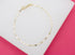 A delicate gold chain bracelet rests on a white display surface against a vibrant pink background.