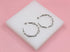 A pair of silver chain link hoop earrings rests on a white display block against a pink background.