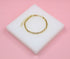 A dainty gold chain link bracelet rests on a square white display block against a soft pink background.