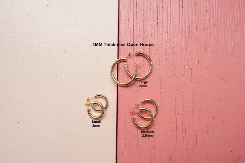 Various sizes of 4mm thick open gold hoop earrings are displayed on a two-toned pink and white background.