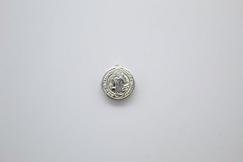 A shiny silver Saint Benedict medal rests centered on a clean, neutral white background.