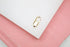A shiny gold lobster clasp rests on a white display surface bordered by a pink background.