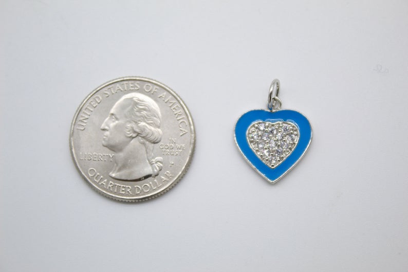 A blue enamel heart charm with sparkling pavé cubic zirconia sits next to a US quarter coin to show its size.