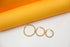 Three graduated sizes of beaded gold hoop earrings rest on a white surface against an orange backdrop.