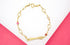 A gold bracelet features alternating oval links and colorful gemstone accents on a pink and white surface.