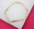 A gold Mariner link bracelet rests on a white display surface against a pink background.