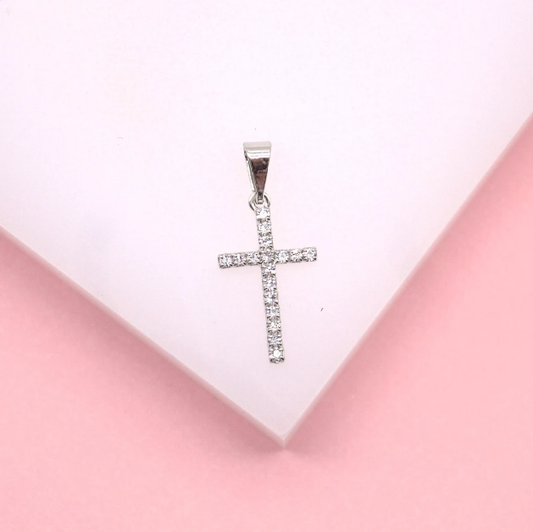 A sparkling diamond cross pendant rests on a soft pink background.