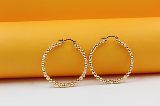 A pair of gold beaded hoop earrings rests against a bright yellow background.