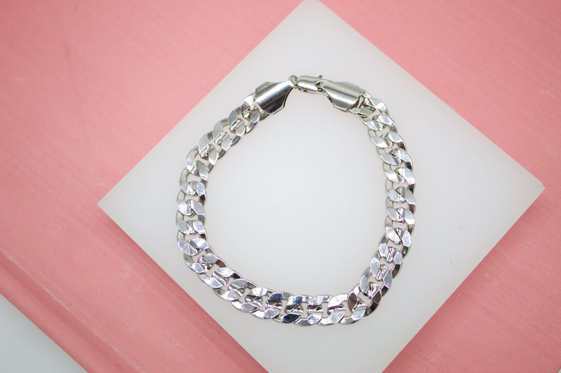 A glossy silver cuban link bracelet rests neatly on a white display pad against a soft pink background.