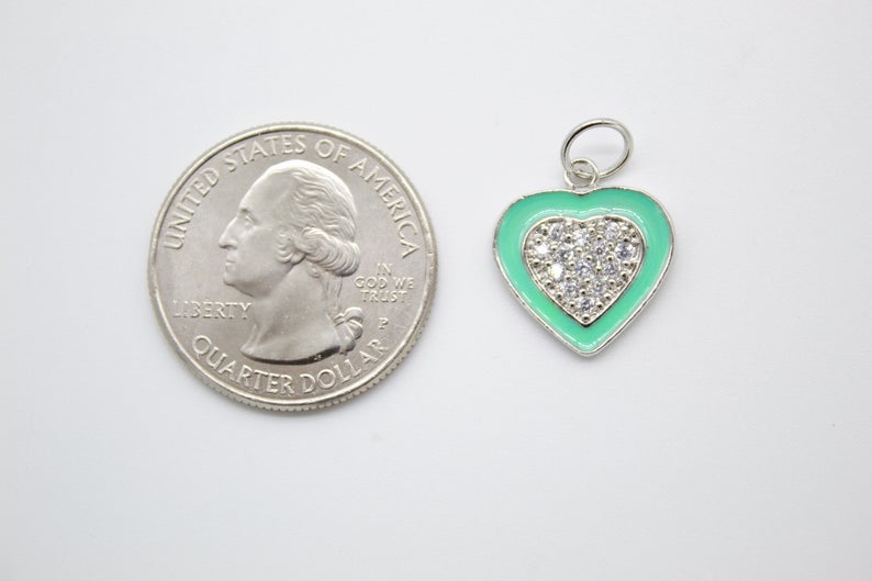 A turquoise enamel and pavé rhinestone heart charm rests next to a US quarter coin for size comparison.