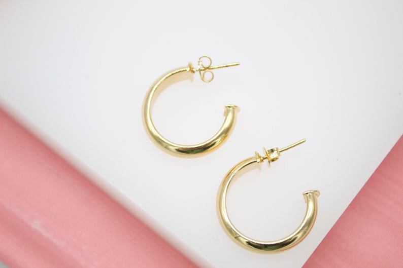 A pair of sleek gold hoop earrings rests against a white and pink display surface.