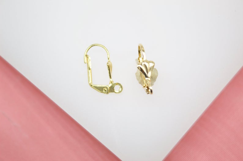 Two shiny gold leverback earring findings lie side by side on a neutral surface.