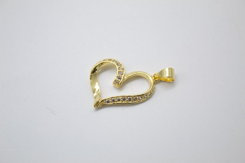 A gold heart-shaped pendant sparkles with embedded cubic zirconia stones against a neutral background.