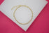 A delicate gold ball chain bracelet rests on a white display stand against a vibrant pink background.