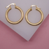 A pair of textured gold hoop earrings rests on a geometric white and pink display.