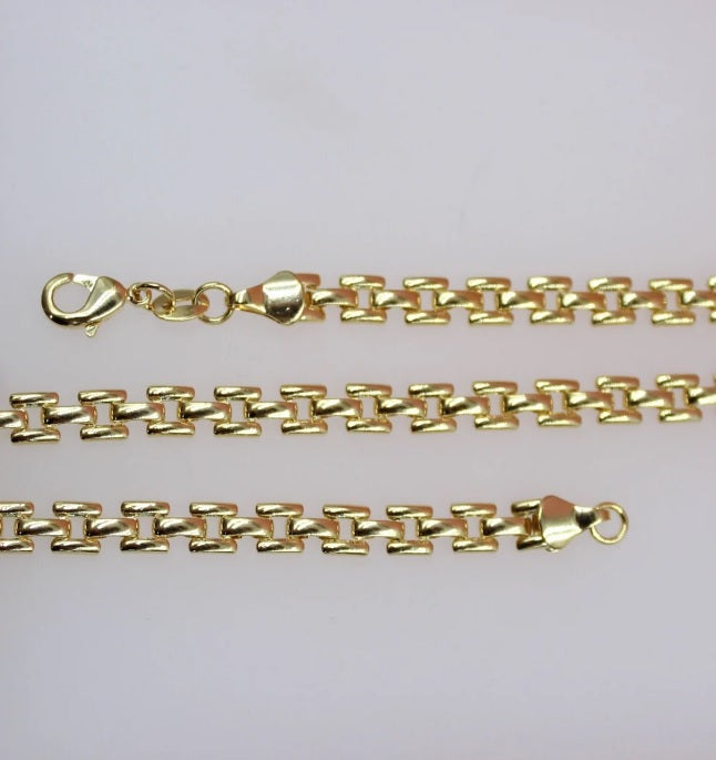 A polished gold link chain rests neatly in rows against a light background, showcasing its intricate geometric design and secure lobster clasp.