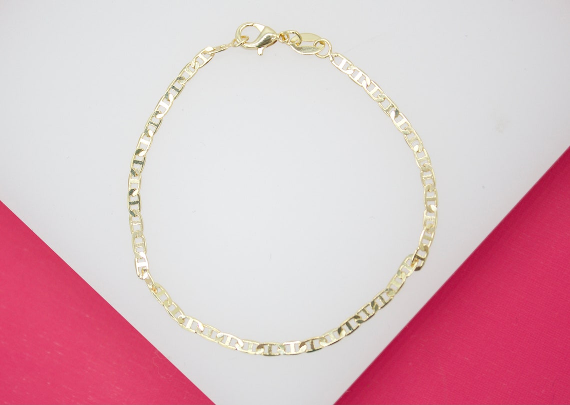 A delicate gold chain bracelet with a classic lobster clasp rests on a white and pink surface.
