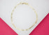 A delicate gold chain bracelet with a classic lobster clasp rests on a white and pink surface.