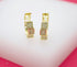 A pair of gold huggie hoop earrings featuring stacked cubic charms encrusted with sparkling micro-pave zirconia stones sits on a white display surface.