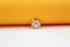 A gold pendant necklace featuring a textured, round compass star charm rests against a vibrant yellow and white background.