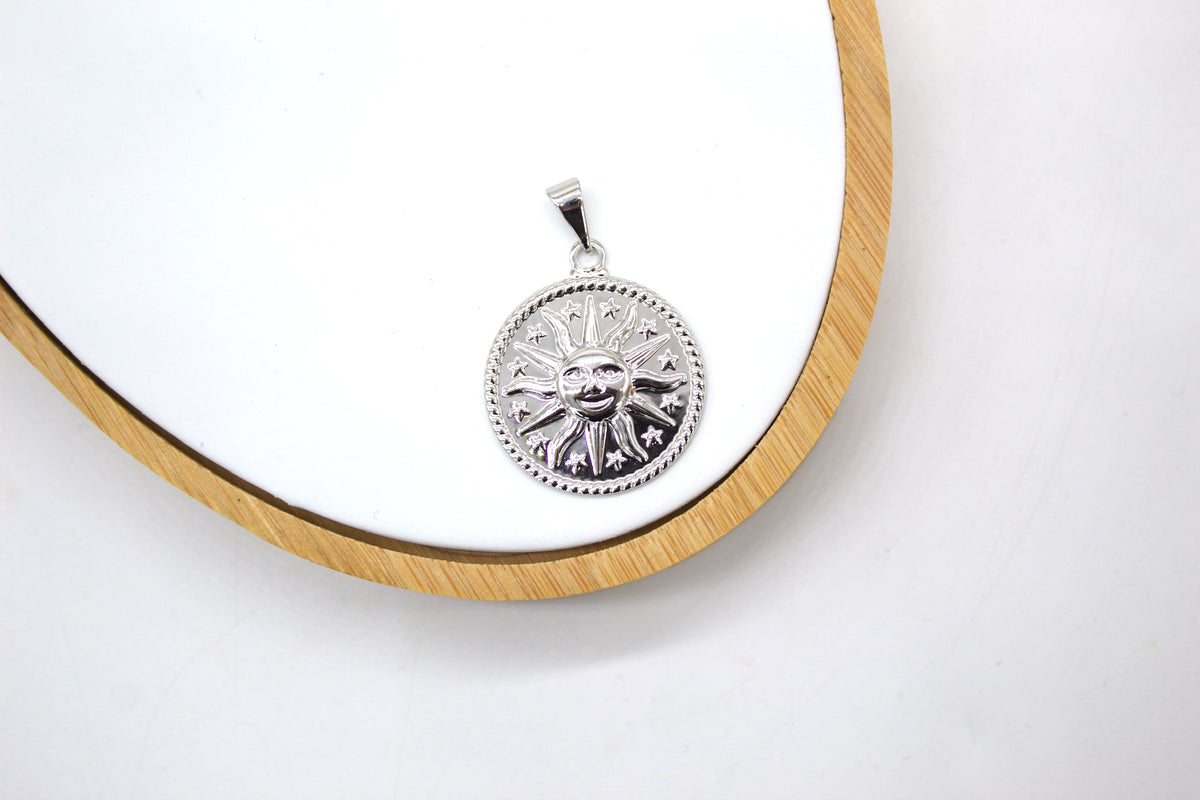 A silver celestial sun pendant rests on a white display board within a wooden circular frame.