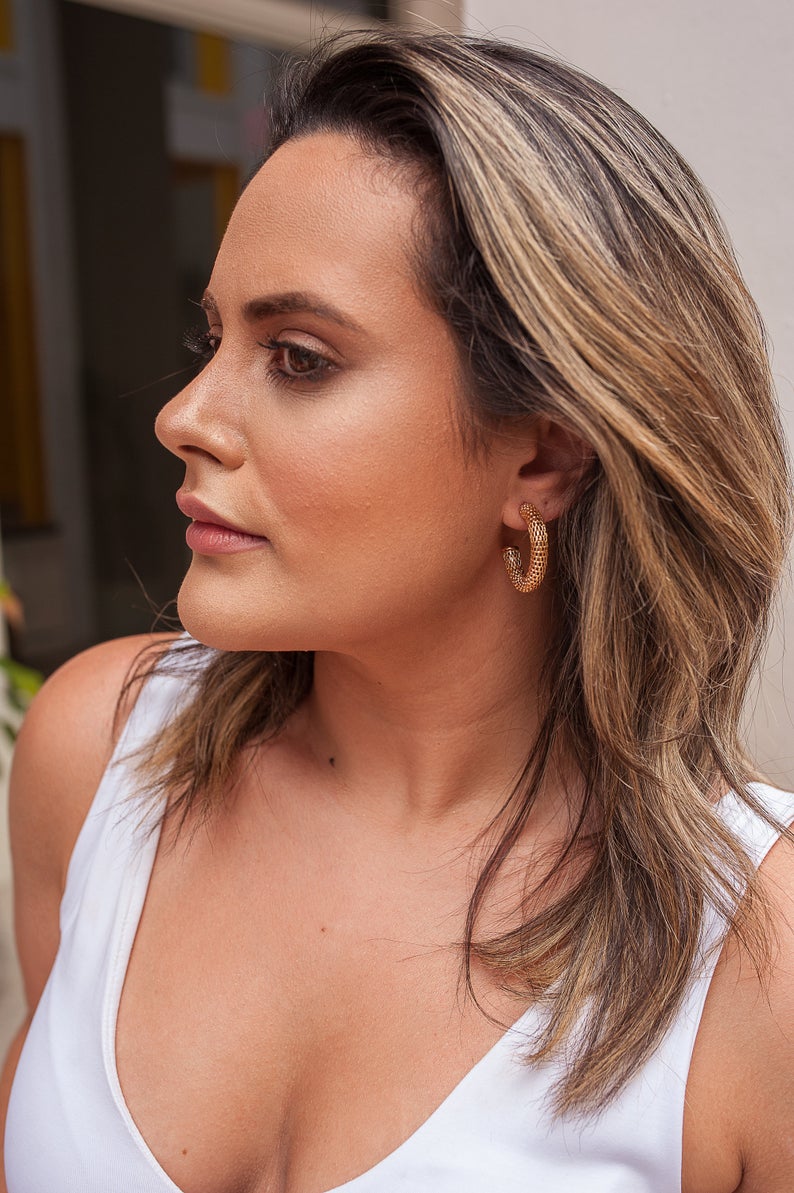 A woman wearing textured gold hoop earrings looks off to the side in profile view.